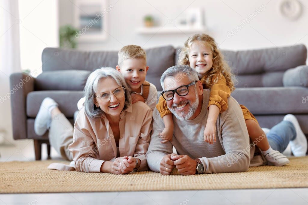 Beautiful cheerful family two cute little kids hugging positive senior grandparents while playing together in living room at home, happy children enjoying time with grandma and grandpa
