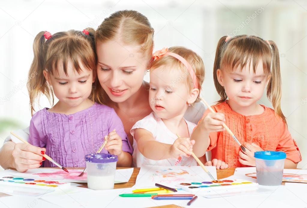 children twin sisters draw paints with her mother in kindergarten