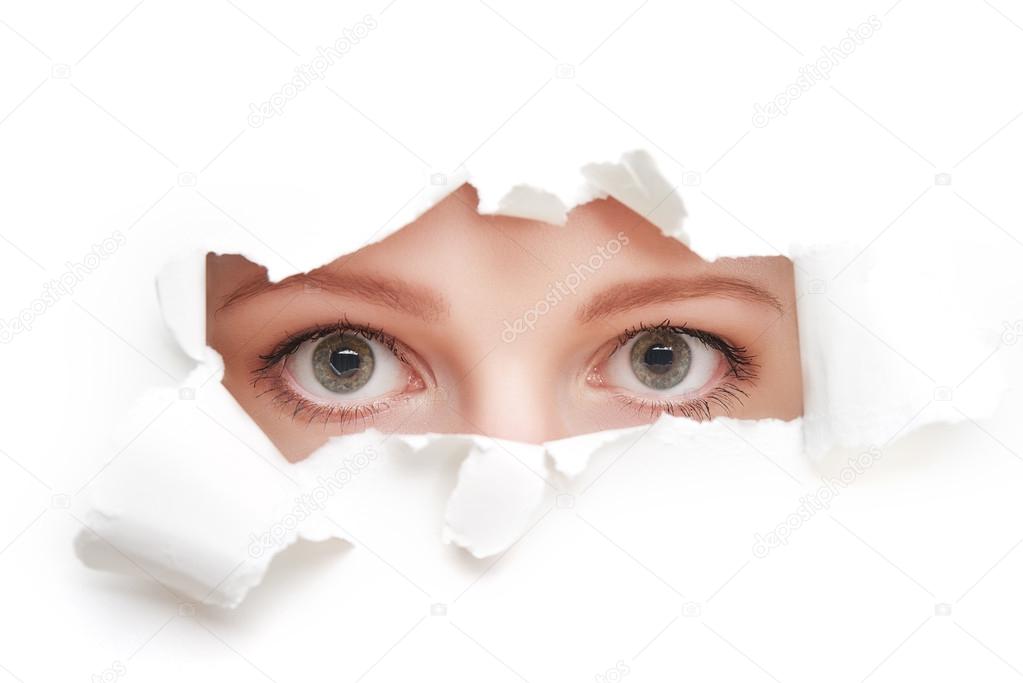 eyes of woman peeking through a  hole torn in white paper poster