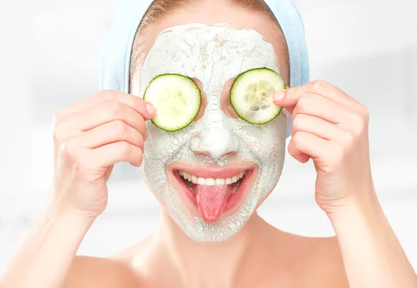 Grappige jong meisje met een masker voor huid gezicht en komkommers — Stockfoto