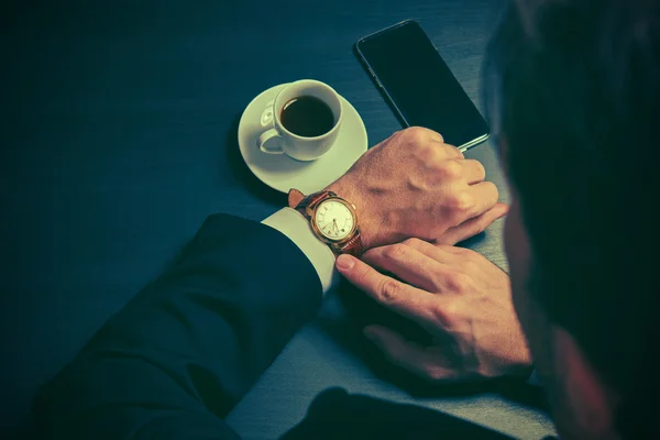 Telefoon en een kopje koffie in de handen van een zakenman in donkere kleuren — Stockfoto