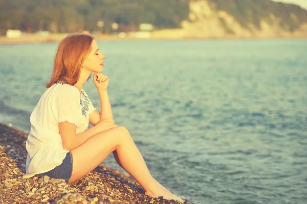 Sad girl sitting on the  beach and looks into the distance at sea — Stock Photo, Image