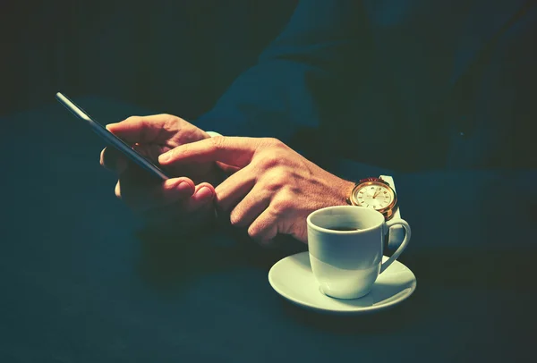 Telefon i filiżankę kawy w rękach biznesmena w ciemnych kolorach — Zdjęcie stockowe