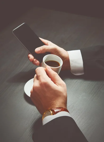 Telefone e uma xícara de café nas mãos de um homem de negócios no escuro — Fotografia de Stock