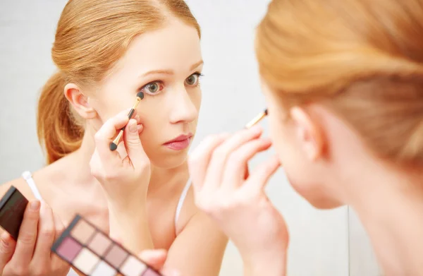 Joven hermosa mujer aplicar maquillaje sombra de ojos frente al espejo — Foto de Stock