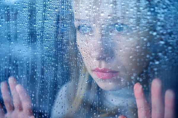 Mujer joven melancólica y triste en la ventana bajo la lluvia —  Fotos de Stock