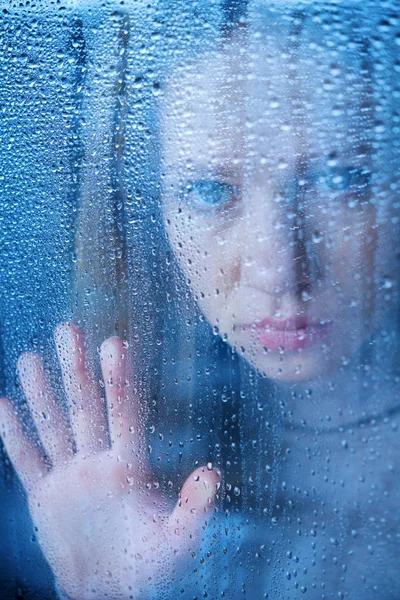 Mujer joven melancólica y triste en la ventana bajo la lluvia — Foto de Stock