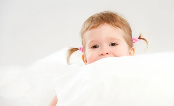 Meisje gluren uit kussens in bed — Stockfoto