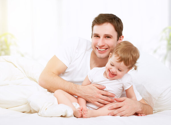 Happy family father and baby  daughter playing in bed