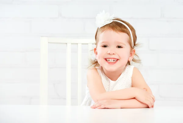 Happy fun funny girl child laughing at  empty white table — Stock Photo, Image