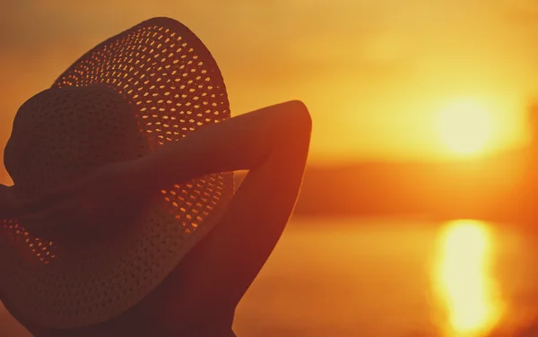 Mujer feliz belleza en su sombrero está de vuelta y admirar la puesta de sol sobre el mar —  Fotos de Stock