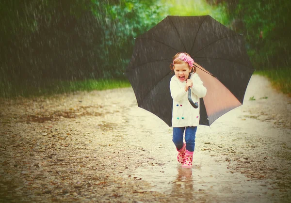 Happy baby girl with an umbrella in the rain runs through — Stockfoto