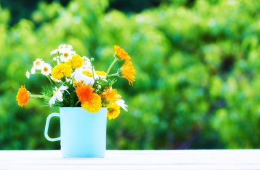 bouquet of wild flowers in  cup on wooden table on a background 