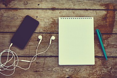 cell phone, headphones, notebook and pen on old wooden table