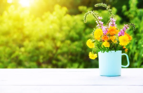 Bouquet of wild flowers in  cup on wooden table on a background — Stock fotografie