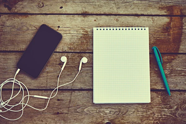 Telefone celular, fones de ouvido, notebook e caneta na mesa de madeira velha — Fotografia de Stock