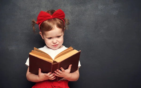 Funny happy  girl schoolgirl with book from blackboard — Stock Photo, Image