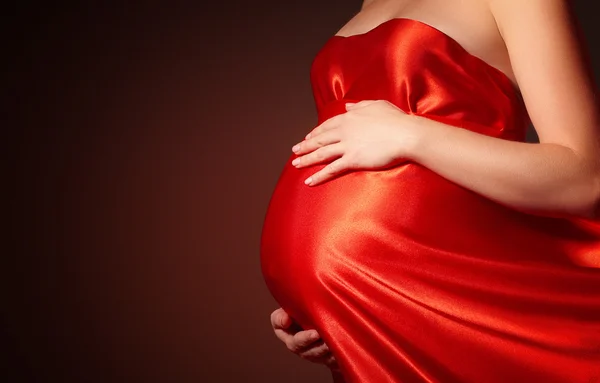 Belly of pregnant woman in  red silk dress billowing Stock Image