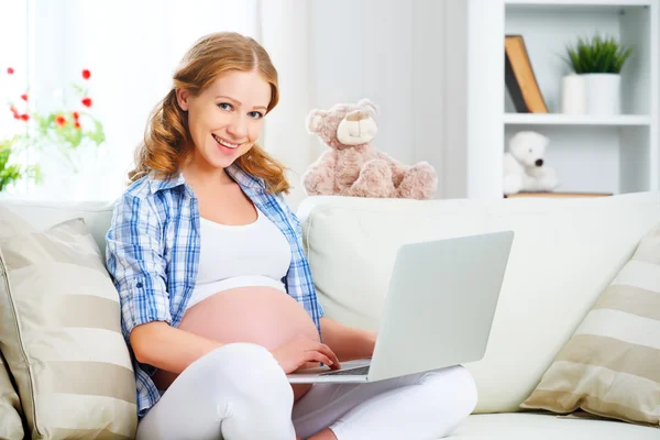 Счастливая беременная женщина с ноутбуком дома — стоковое фото