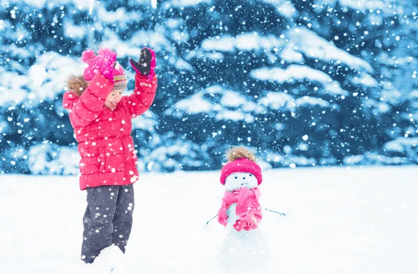 Happy child girl with a snowman on a winter walk — Stock Photo, Image