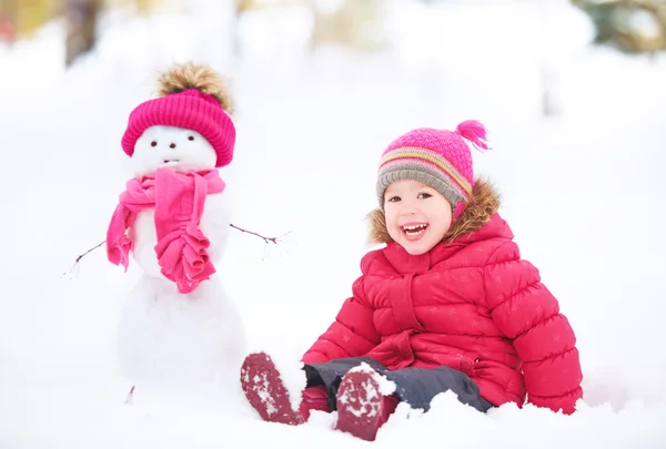 Menina criança feliz com um boneco de neve em uma caminhada de inverno — Fotografia de Stock