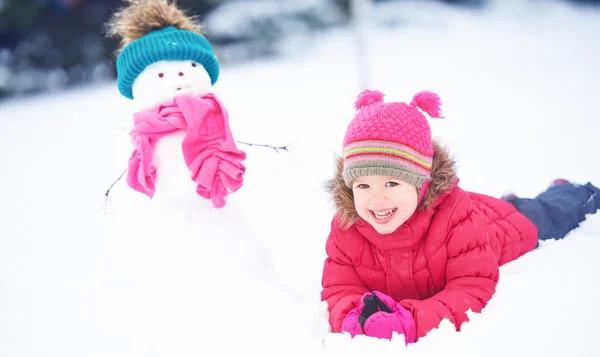 Menina criança feliz com um boneco de neve em uma caminhada de inverno — Fotografia de Stock