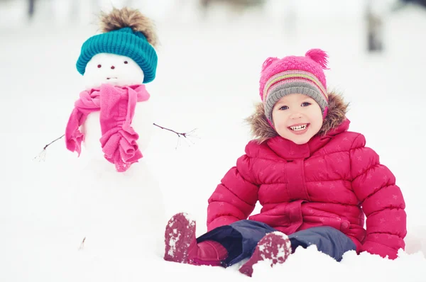 Happy child girl with a snowman on a winter walk — Stock Photo, Image