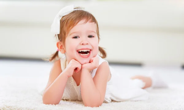 Happy little girl lying on floor in a white room — Stock Photo, Image