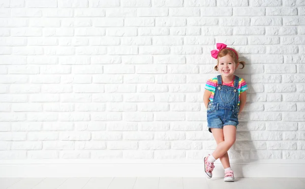 Lyckligt barn lilla flickan skrattar åt Tom tegelvägg — Stockfoto