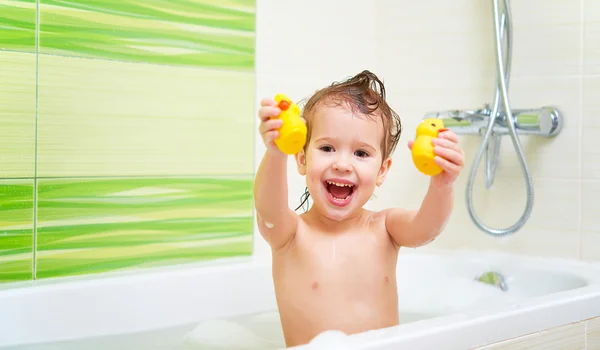 Criança feliz com brinquedos de pato amarelo banha-se no banho com espuma e — Fotografia de Stock