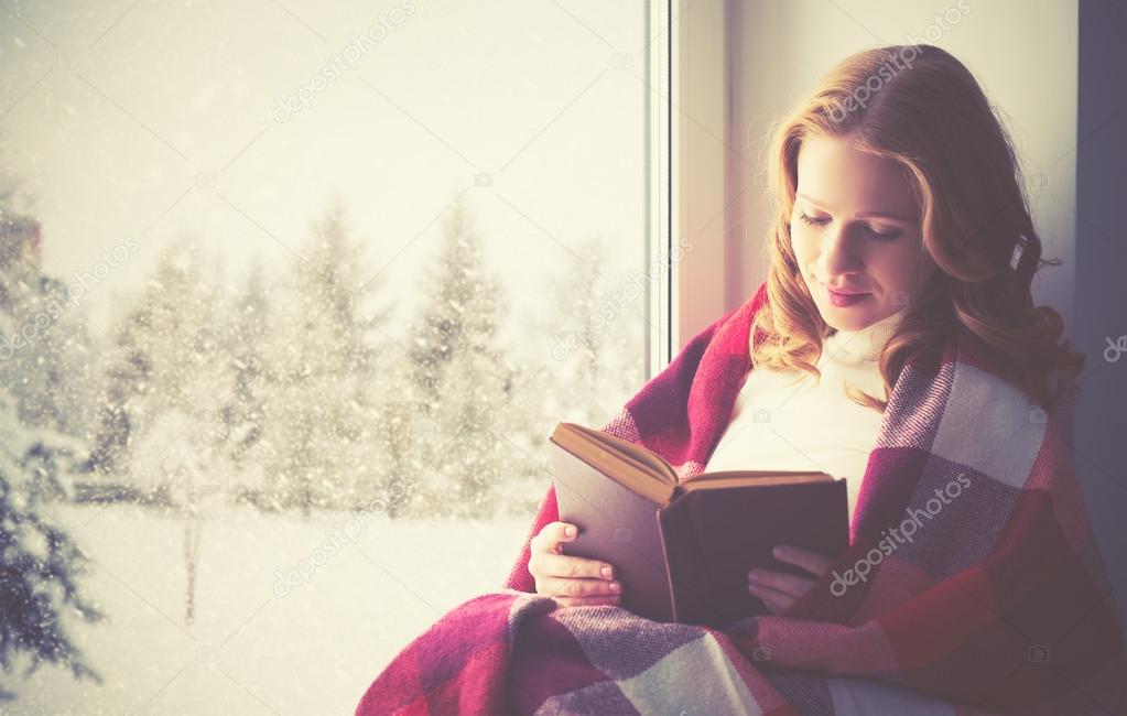 happy girl reading book by the window in winter