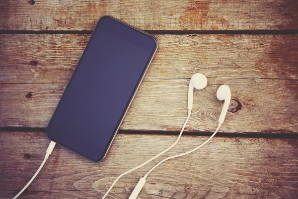 Cell phone and headphones lay on old wooden table — Stock Photo, Image