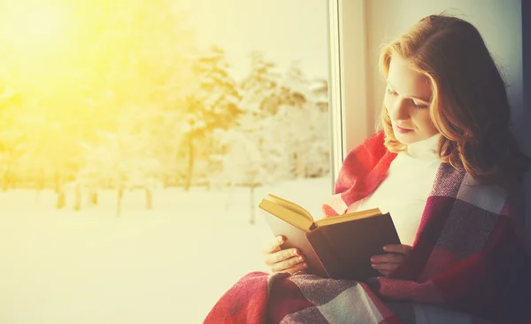 Feliz niña leyendo libro por la ventana en invierno — Foto de Stock