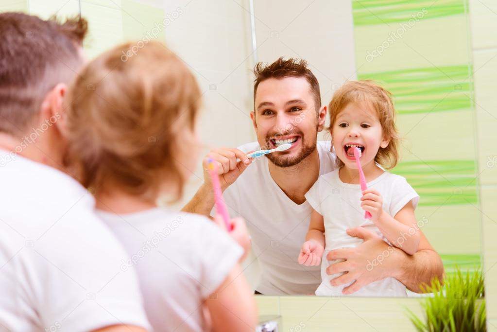 Happy family father and child girl brushing her teeth in bathroo