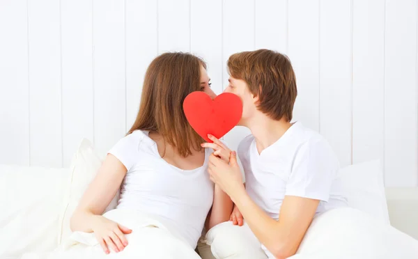 Amante casal beijos com um coração vermelho na cama — Fotografia de Stock