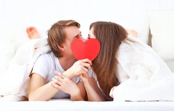 Amante casal beijos com um coração vermelho na cama — Fotografia de Stock