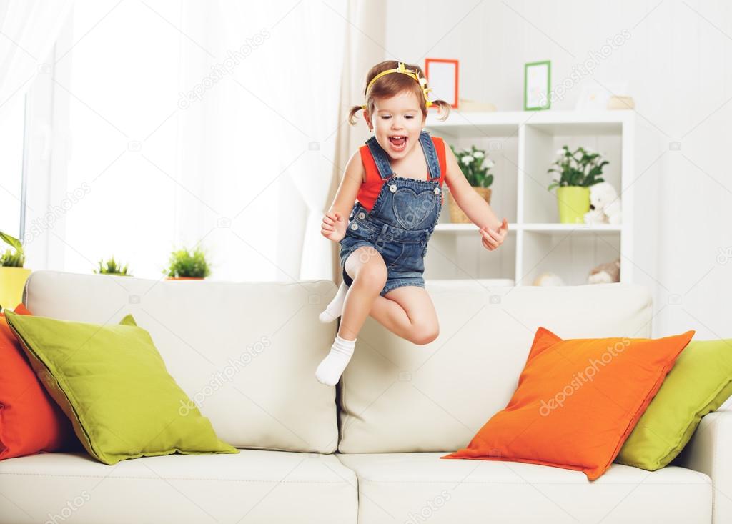 happy child girl playing and jumping on couch at home