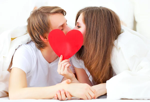 Minnaar paar zoenen met een rood hart in bed — Stockfoto