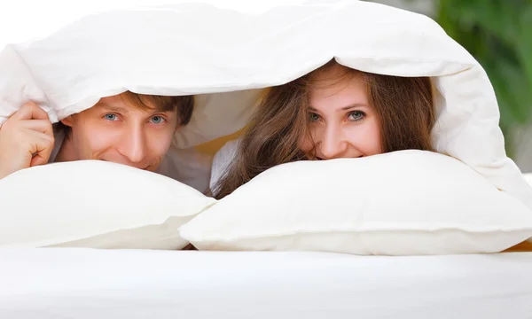 Joyeux couple riant au lit regardant sous la couverture — Photo