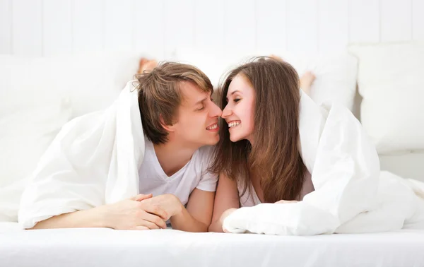 Casal feliz rindo na cama espreitando debaixo do cobertor — Fotografia de Stock