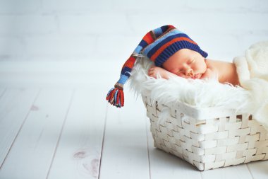 Mavi örgü şapkalı sepet içinde uyuyan sevimli bebek