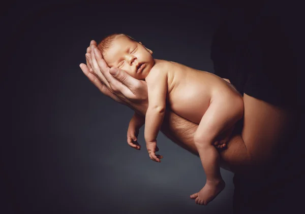 Pasgeboren baby slapen in de handen van zijn vader op een donker — Stockfoto