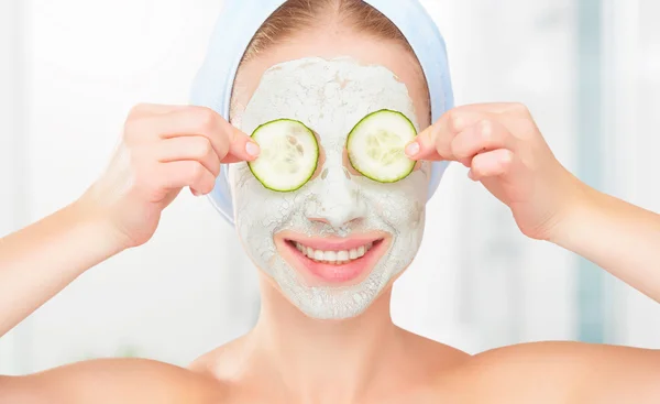 Grappige jong meisje met een masker voor huid gezicht en komkommers — Stockfoto