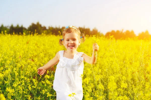 Glad liten barn flicka kör på fältet med gula blommor — Stockfoto