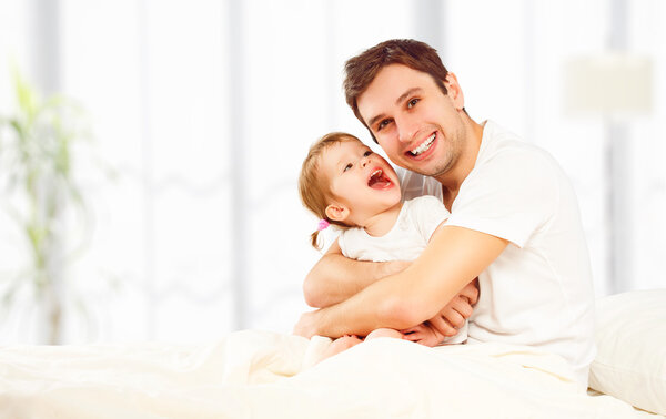 Happy family father and child  daughter playing in bed