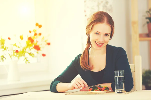 Молодая здоровая женщина ест овощи дома на кухне — стоковое фото