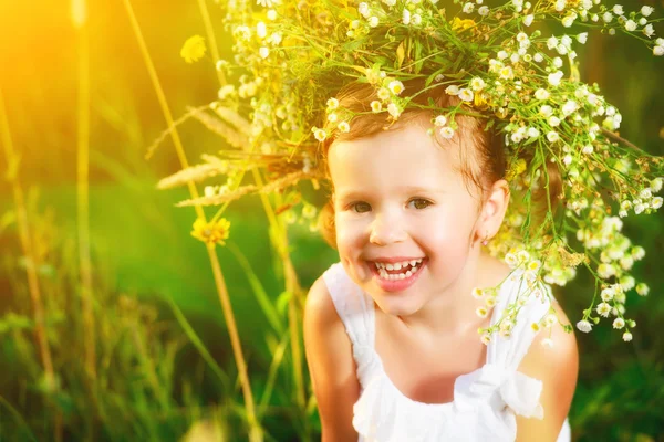 Funny happy baby girl in a wreath on nature laughing in su — стоковое фото