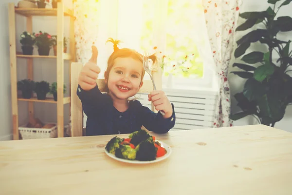 Bambino felice ragazza ama mangiare verdure e mostrando pollici in su — Foto Stock