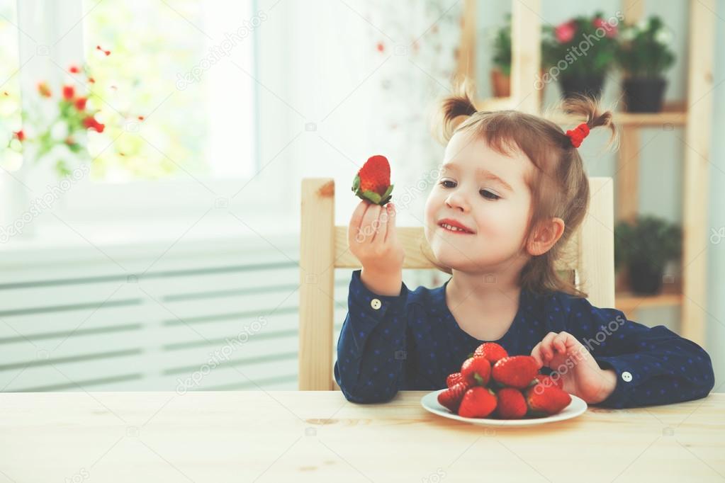 happy child girl eats strawberries in summer home kitchen