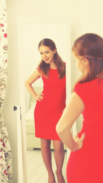 Mujer en un vestido rojo se mira en el espejo —  Fotos de Stock